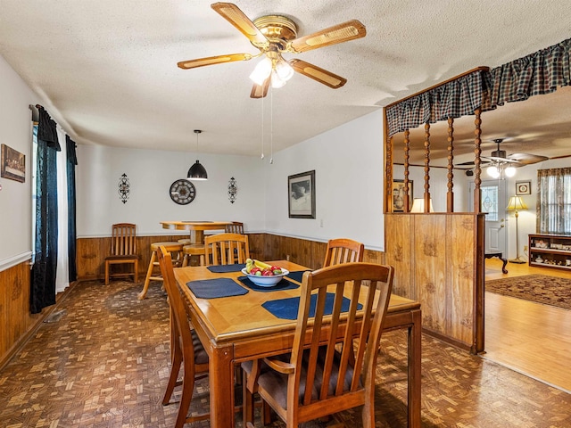 dining area with a textured ceiling, ceiling fan, wooden walls, and parquet floors