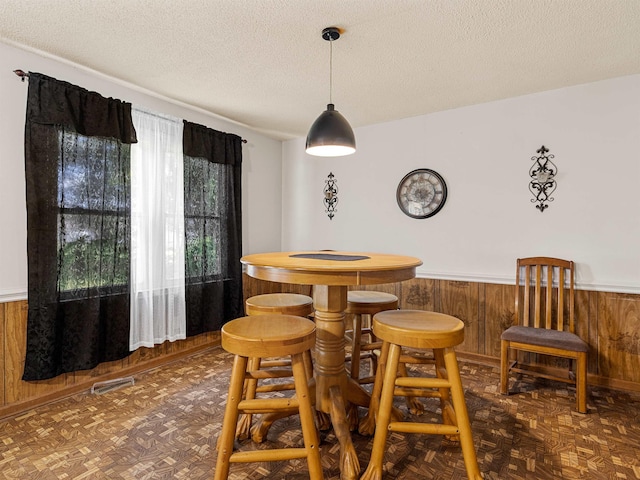 dining area with dark parquet flooring, a textured ceiling, and wood walls