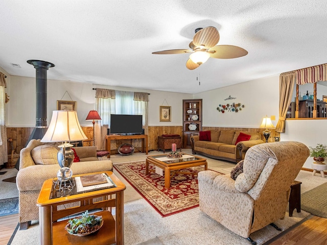 living room featuring wooden walls, a textured ceiling, ceiling fan, and light wood-type flooring