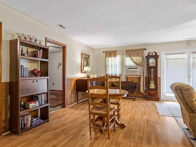 dining area featuring cooling unit, wood walls, light wood-type flooring, and a textured ceiling