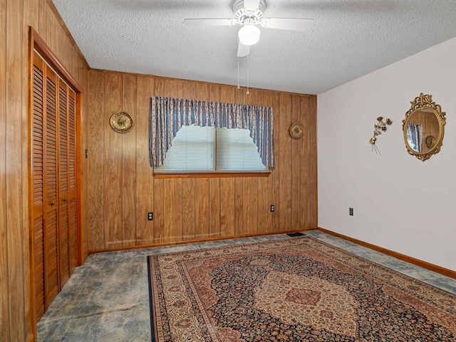 spare room with a textured ceiling, wood walls, and ceiling fan