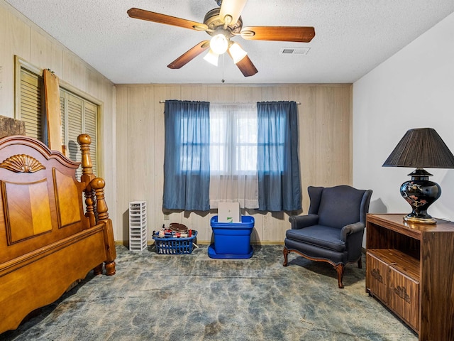 living area with a textured ceiling, wood walls, ceiling fan, and dark colored carpet