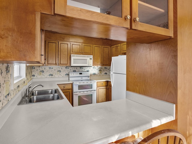 kitchen featuring white appliances, a breakfast bar, kitchen peninsula, and sink