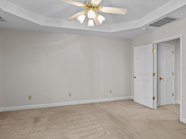 spare room with ceiling fan, light carpet, and a raised ceiling