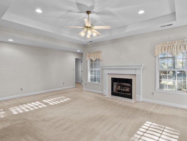 unfurnished living room with a fireplace, ceiling fan, a tray ceiling, and light carpet