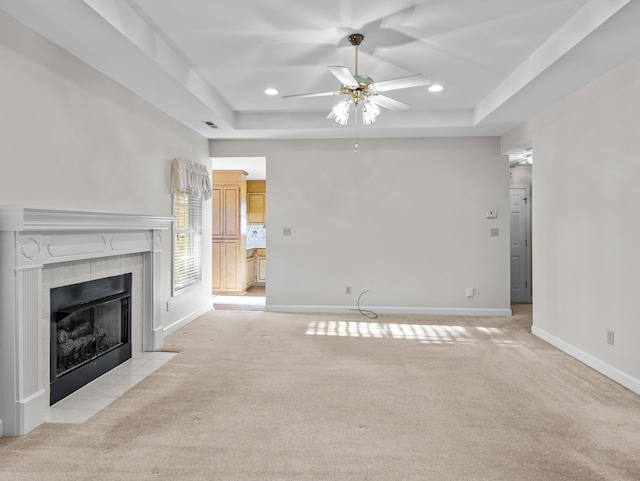 unfurnished living room featuring ceiling fan, light colored carpet, a raised ceiling, and a fireplace