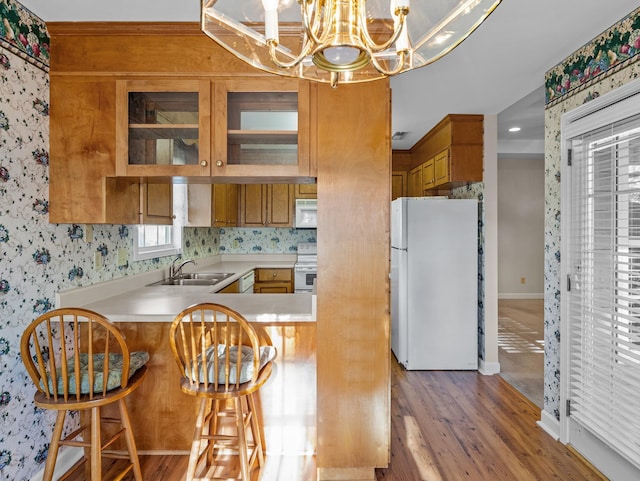 kitchen with sink, an inviting chandelier, white appliances, kitchen peninsula, and a breakfast bar