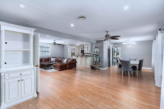 living room with a textured ceiling, light wood-type flooring, and ceiling fan with notable chandelier