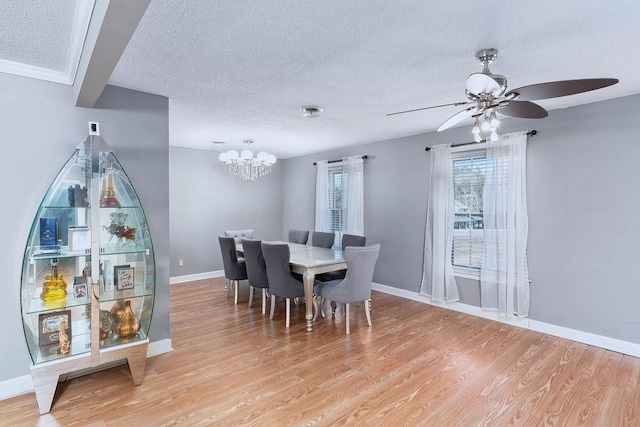 dining room with ceiling fan with notable chandelier, a textured ceiling, and light hardwood / wood-style flooring