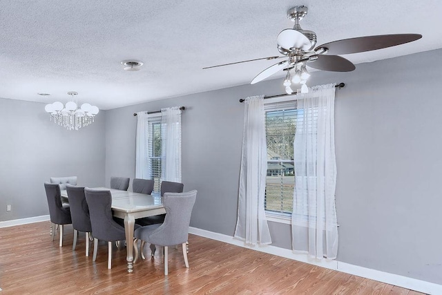 dining space with ceiling fan with notable chandelier, wood-type flooring, and a textured ceiling