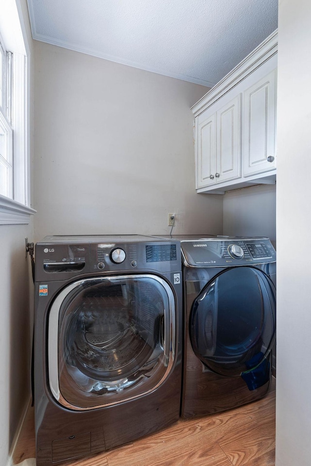 clothes washing area with washing machine and clothes dryer, light wood-type flooring, and cabinets