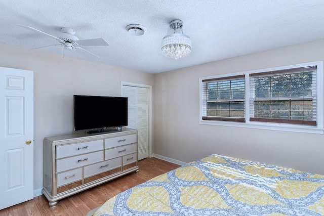 bedroom featuring ceiling fan with notable chandelier, hardwood / wood-style flooring, a textured ceiling, and a closet