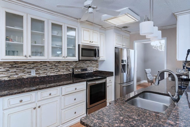 kitchen featuring dark stone countertops, stainless steel appliances, ornamental molding, pendant lighting, and sink