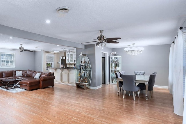 dining space featuring a textured ceiling, light wood-type flooring, and ceiling fan with notable chandelier