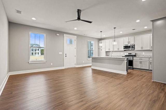 kitchen with a center island with sink, appliances with stainless steel finishes, light stone countertops, pendant lighting, and dark hardwood / wood-style floors