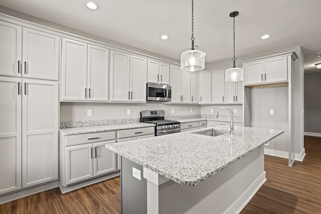 kitchen with sink, pendant lighting, light stone countertops, a kitchen island with sink, and appliances with stainless steel finishes