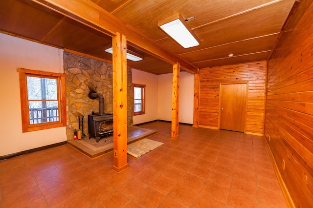 basement featuring wooden walls, wooden ceiling, a wealth of natural light, and a wood stove