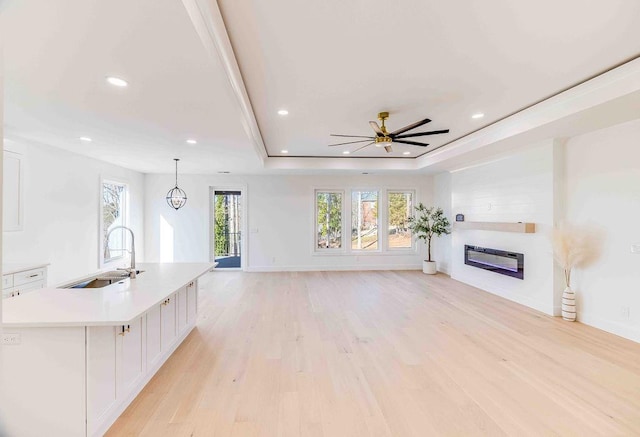 unfurnished living room featuring sink, light hardwood / wood-style floors, a raised ceiling, and ceiling fan with notable chandelier