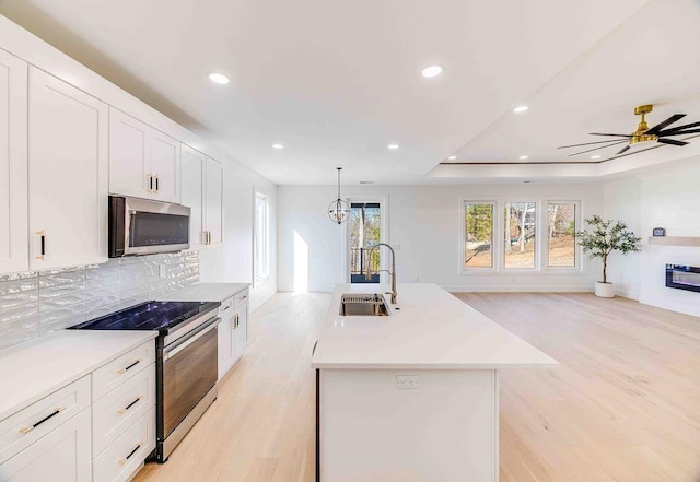 kitchen with stainless steel appliances, pendant lighting, an island with sink, and white cabinetry