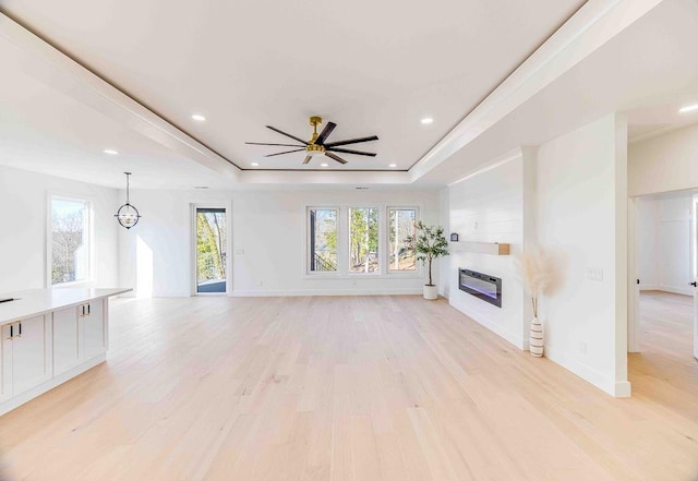 unfurnished living room with ceiling fan with notable chandelier, a raised ceiling, light hardwood / wood-style flooring, and heating unit