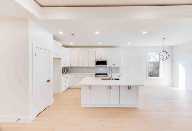 kitchen featuring a center island with sink, pendant lighting, sink, white cabinetry, and an inviting chandelier