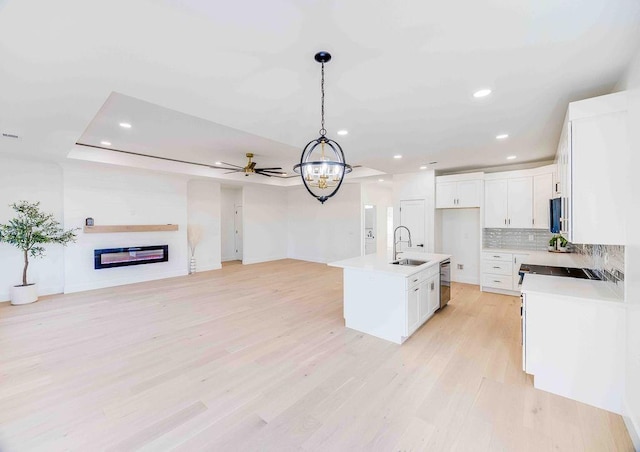 kitchen with sink, an island with sink, hanging light fixtures, and white cabinetry