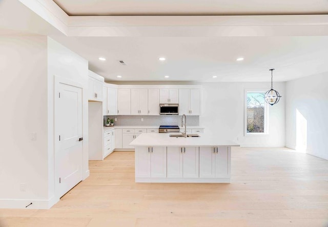 kitchen featuring stainless steel appliances, sink, white cabinets, pendant lighting, and a kitchen island with sink