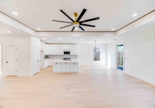 kitchen with light hardwood / wood-style flooring, a kitchen island with sink, a tray ceiling, white cabinetry, and ceiling fan