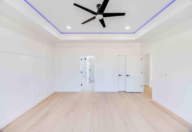 spare room with ceiling fan, a tray ceiling, and light hardwood / wood-style flooring