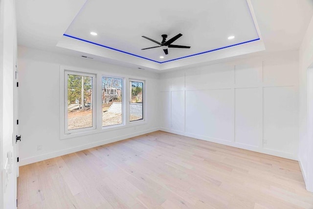 empty room featuring light wood-type flooring, a raised ceiling, and ceiling fan