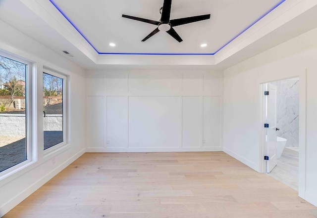 spare room featuring ceiling fan, light wood-type flooring, and a raised ceiling