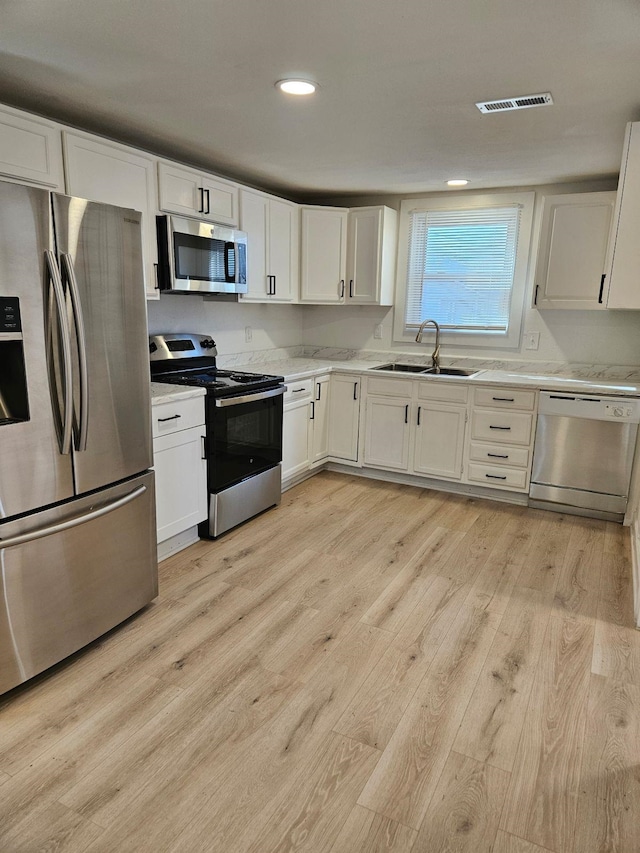 kitchen with sink, white cabinetry, appliances with stainless steel finishes, and light wood-type flooring