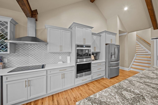 kitchen featuring light hardwood / wood-style floors, appliances with stainless steel finishes, decorative backsplash, wall chimney range hood, and beamed ceiling