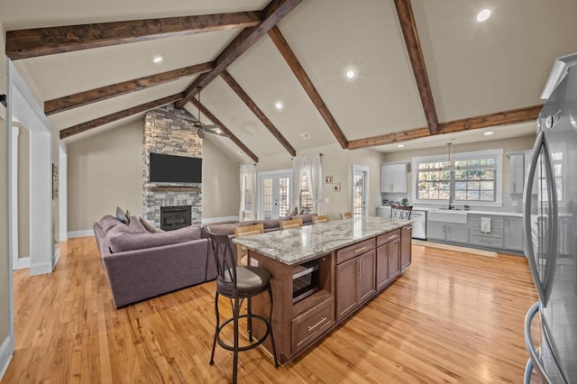 kitchen with a stone fireplace, ceiling fan, appliances with stainless steel finishes, light hardwood / wood-style flooring, and a center island