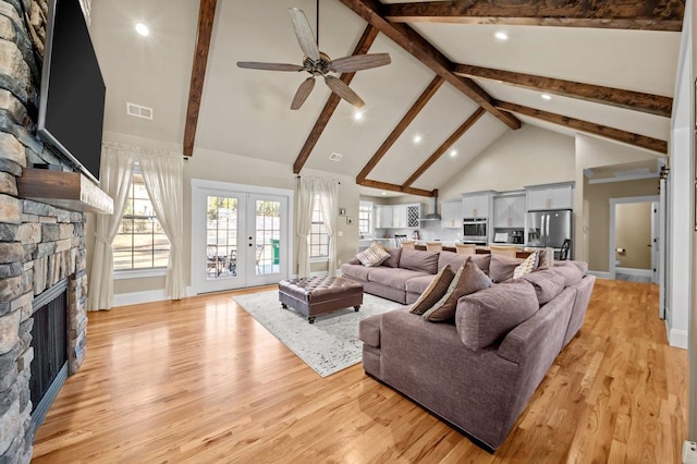 living room with beamed ceiling, light hardwood / wood-style flooring, a stone fireplace, high vaulted ceiling, and french doors