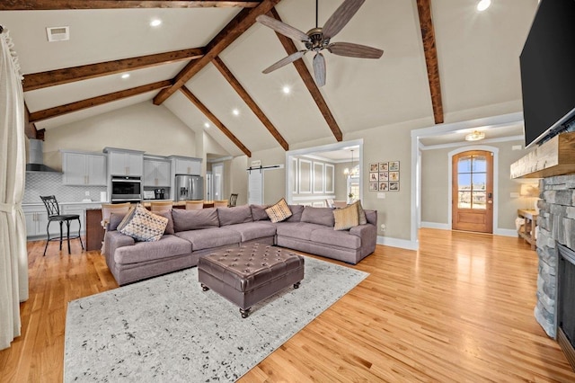 living room with high vaulted ceiling, ceiling fan with notable chandelier, a stone fireplace, and light hardwood / wood-style floors