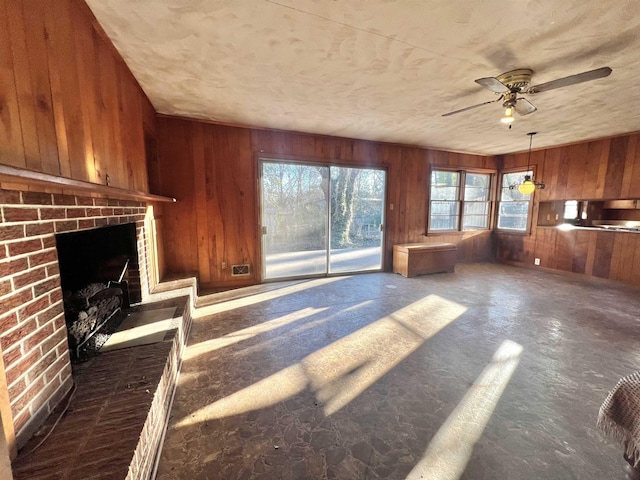 unfurnished living room featuring a brick fireplace, ceiling fan, and wooden walls