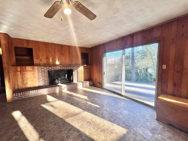 unfurnished living room featuring ceiling fan, a fireplace, and wooden walls