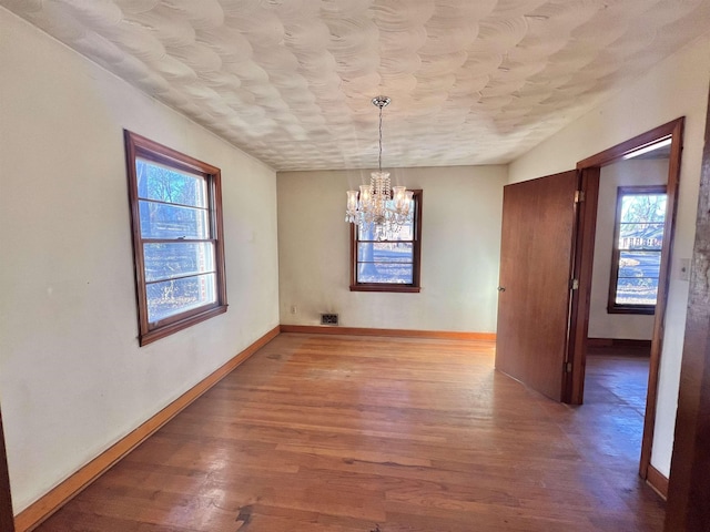 unfurnished dining area with wood-type flooring and an inviting chandelier