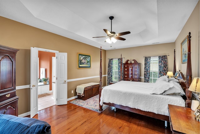 bedroom with ceiling fan, ensuite bathroom, hardwood / wood-style floors, and a tray ceiling