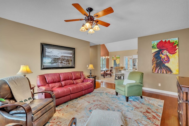 living room with vaulted ceiling, ceiling fan with notable chandelier, and hardwood / wood-style flooring