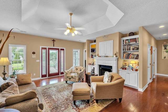 living room featuring a raised ceiling, ceiling fan, dark hardwood / wood-style floors, and a textured ceiling