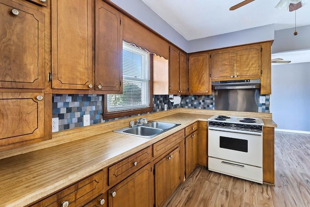 kitchen with white stove, decorative backsplash, light hardwood / wood-style flooring, and sink