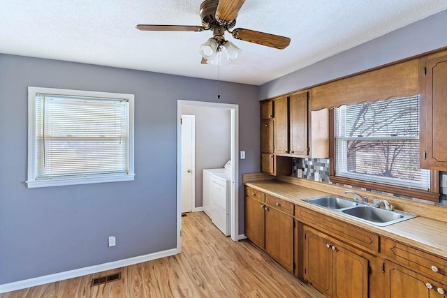 kitchen featuring washer / dryer, light hardwood / wood-style floors, ceiling fan, decorative backsplash, and sink