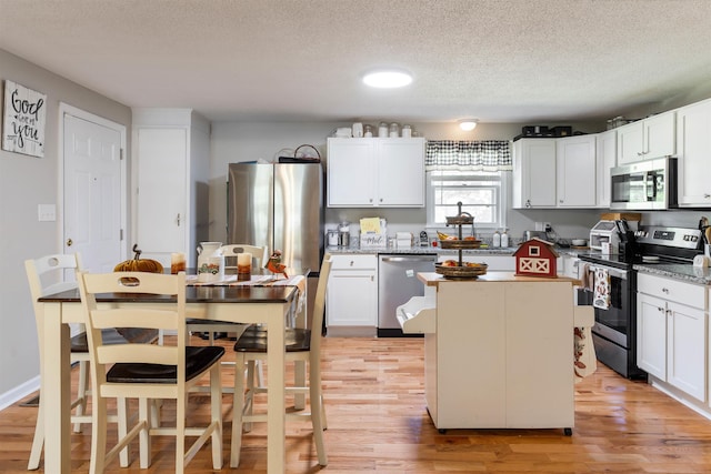 kitchen with white cabinetry, a center island, stainless steel appliances, and light hardwood / wood-style flooring