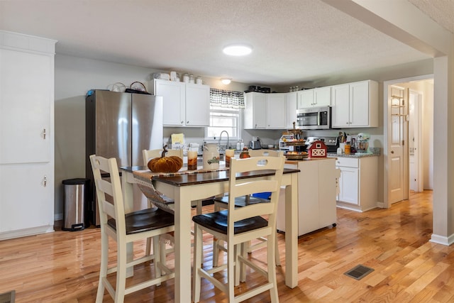 kitchen with light hardwood / wood-style floors, appliances with stainless steel finishes, white cabinetry, and a textured ceiling