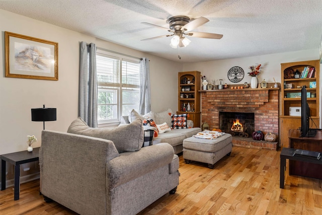 living room featuring a textured ceiling, ceiling fan, light hardwood / wood-style floors, and a brick fireplace