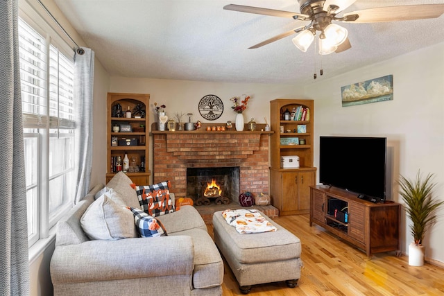 living room featuring ceiling fan, a brick fireplace, a textured ceiling, and light hardwood / wood-style floors