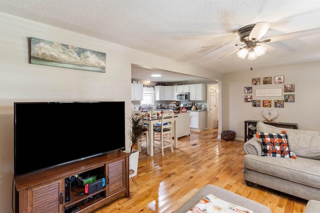 living room with ceiling fan, sink, a textured ceiling, and light hardwood / wood-style floors