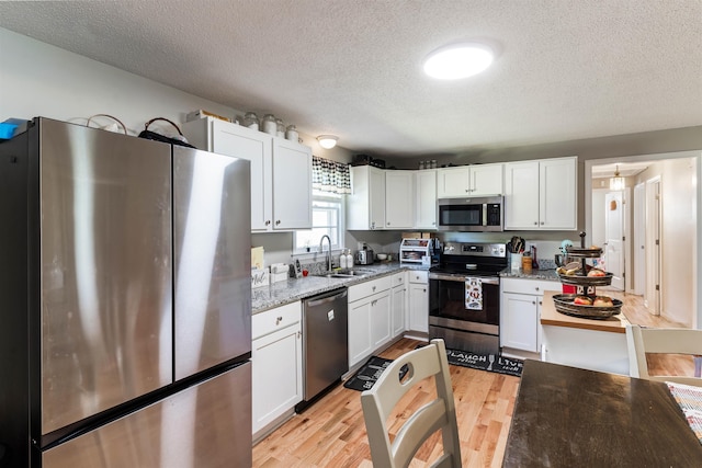 kitchen featuring appliances with stainless steel finishes, light stone countertops, a textured ceiling, white cabinets, and sink